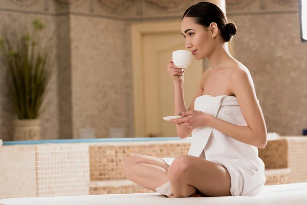 Belle asiatique femme dans serviette boire café à spa — Photo de stock