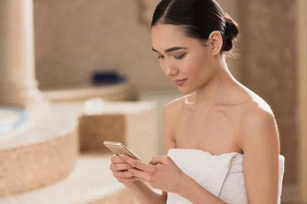 Attractive asian woman in towel using smartphone at spa — Stock Photo