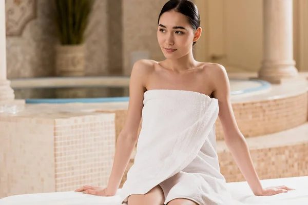 Attractive asian woman in towel relaxing and looking away at spa — Stock Photo