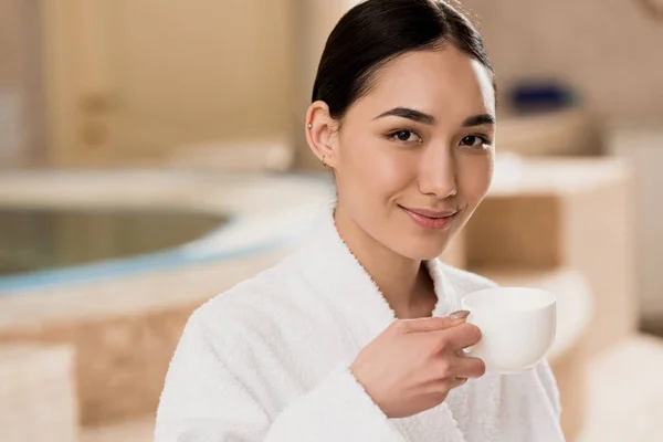 Beautiful asian woman in bathrobe drinking coffee at spa — Stock Photo