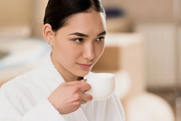 Attractive asian woman in bathrobe drinking coffee at spa — Stock Photo