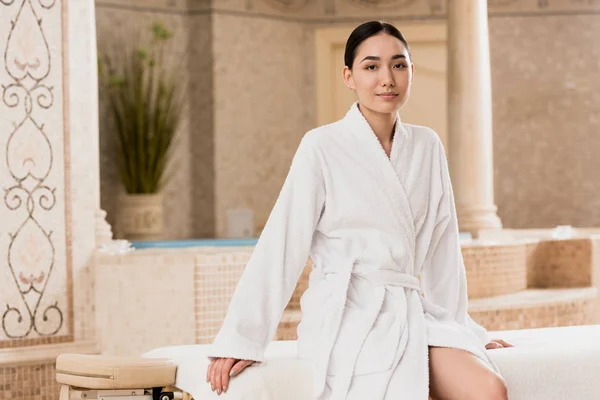 Bela asiática mulher no roupão de banho sentado e olhando para a câmera — Fotografia de Stock