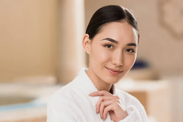 Attractive asian woman in bathrobe looking at camera at spa — Stock Photo