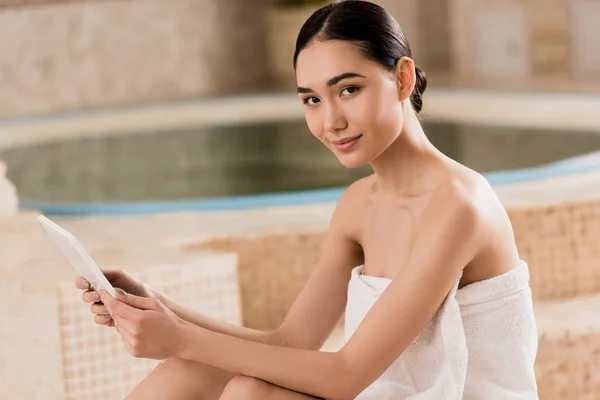 Atractivo asiático mujer en toalla celebración digital tablet y mirando a cámara - foto de stock