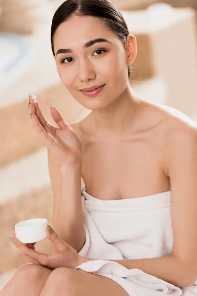 Hermosa mujer asiática en toalla aplicando crema cosmética en spa - foto de stock