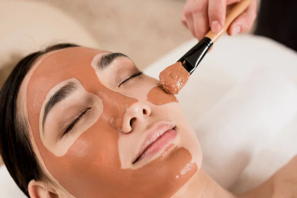 Обрезанный вид косметолога, надевающего маску на красивое лицо женщины — стоковое фото