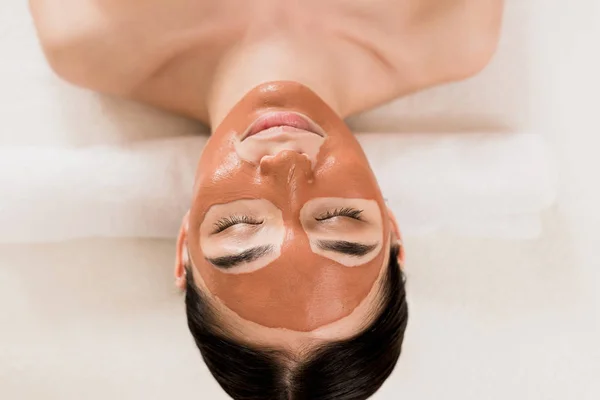 Beautiful woman lying with clay mask on face at spa — Stock Photo