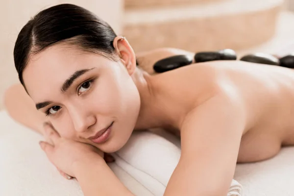 Beautiful woman getting stone massage and looking at camera at spa — Stock Photo