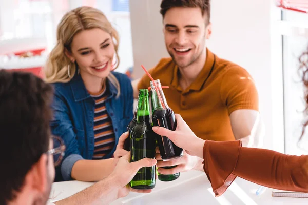 Enfoque selectivo de amigos sonrientes animando con soda y cerveza en la cafetería - foto de stock