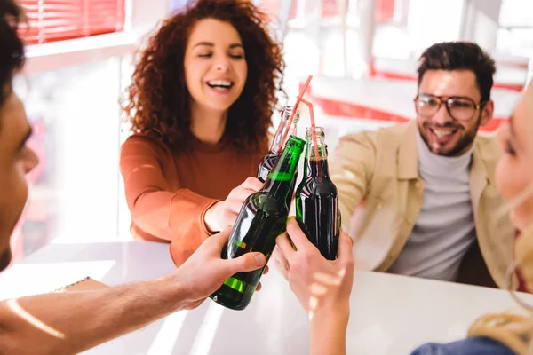 Selective focus of smiling and beautiful friends cheering with soda and beer at cafe — Stock Photo