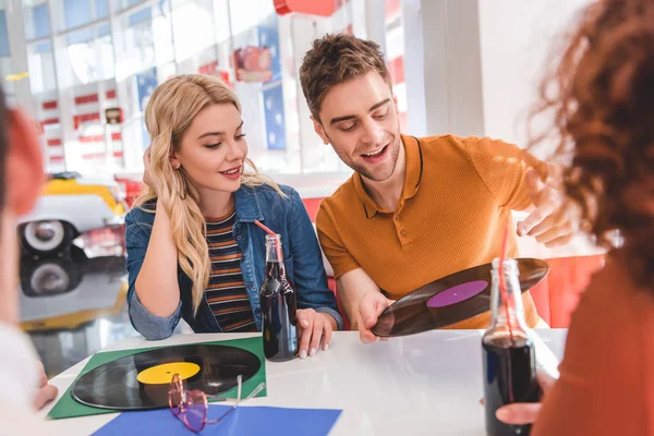Selective focus of handsome and attractive friends talking and holding vinyl at cafe — Stock Photo