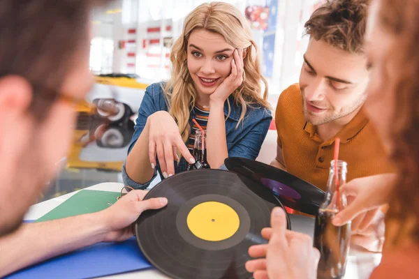 Foco seletivo de amigos sorridentes, bonitos e bonitos conversando e segurando vinil no café — Fotografia de Stock