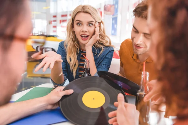 Enfoque selectivo de sonreír, amigos guapos y atractivos hablando y sosteniendo vinilo en la cafetería - foto de stock