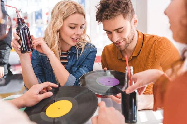 Selective focus of handsome and beautiful friends talking, holding vinyl and glass bottles with drink — Stock Photo