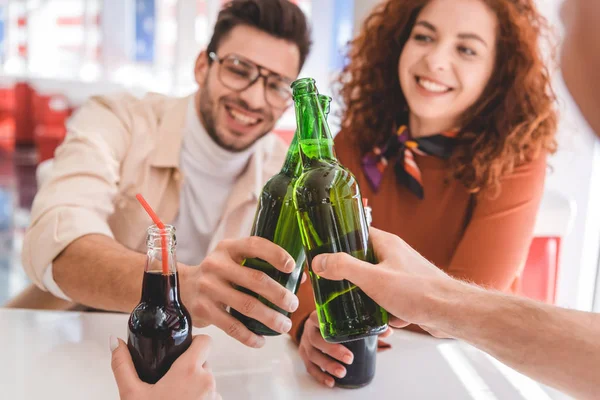 Selective focus of glass bottles with beverage holding by friends — Stock Photo