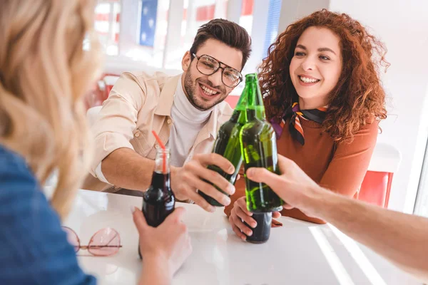 Enfoque selectivo de guapos y hermosos amigos animando con botellas de vidrio y sonriendo - foto de stock