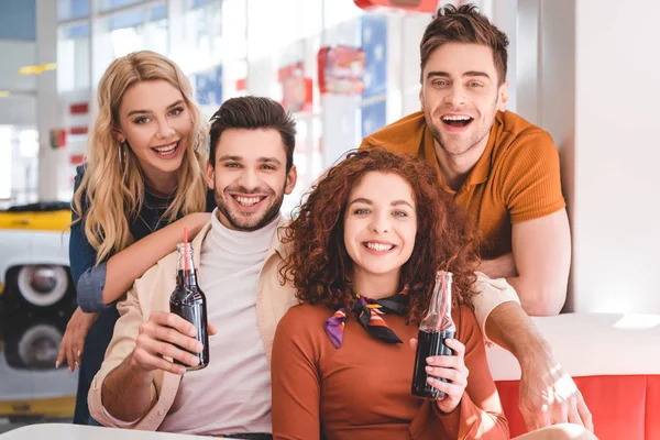 Schöne und schöne Freunde, die Glasflaschen mit Getränken in der Hand halten und in die Kamera schauen — Stockfoto