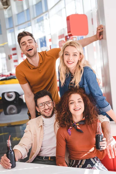 Amigos guapos y atractivos sosteniendo botellas de vidrio con bebida y sonriendo - foto de stock