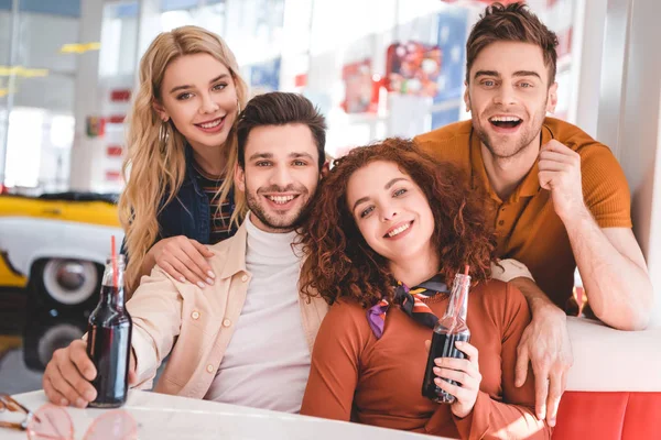 Amigos guapos y atractivos sosteniendo botellas de vidrio con soda y sonriendo — Stock Photo