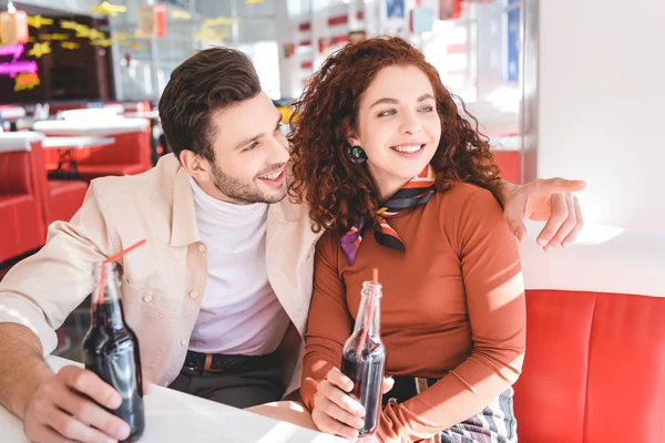 Couple smiling, holding glass bottles with soda and looking away — Stock Photo