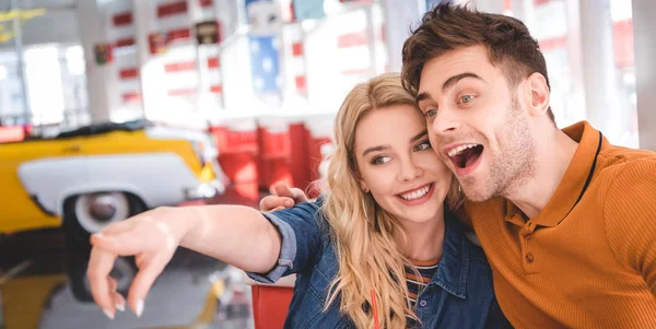 Hermosa mujer señalando con el dedo y el hombre sonriendo y mirando hacia otro lado en la cafetería - foto de stock