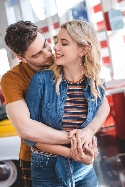 Hermosa pareja sonriendo, mirándose y abrazándose en la cafetería - foto de stock