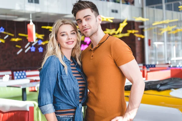 Hermosa pareja sonriendo, mirando a la cámara y abrazándose en la cafetería - foto de stock