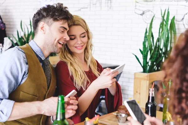 Selective focus of beautiful couple smiling and using digital devices at cafe — Stock Photo