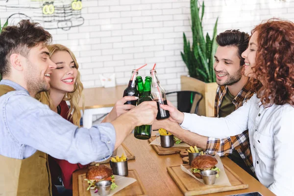 Handsome and beautiful friends cheering with glass bottles at cafe — Stock Photo