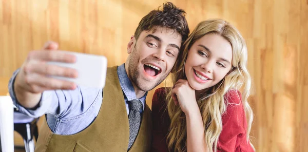 Enfoque selectivo de hombre guapo y hermosa mujer tomando selfie en la cafetería - foto de stock