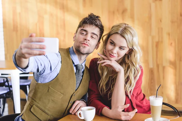 Enfoque selectivo de hombre guapo y mujer atractiva tomando selfie en la cafetería - foto de stock