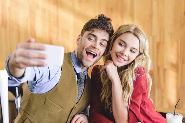 Selective focus of beautiful and smiling couple taking selfie with smartphone at cafe — Stock Photo