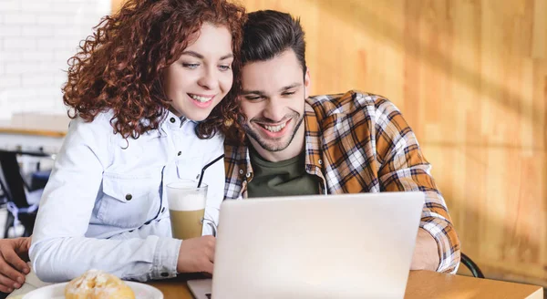 Beautiful and smiling couple hugging and using laptop at cafe — Stock Photo