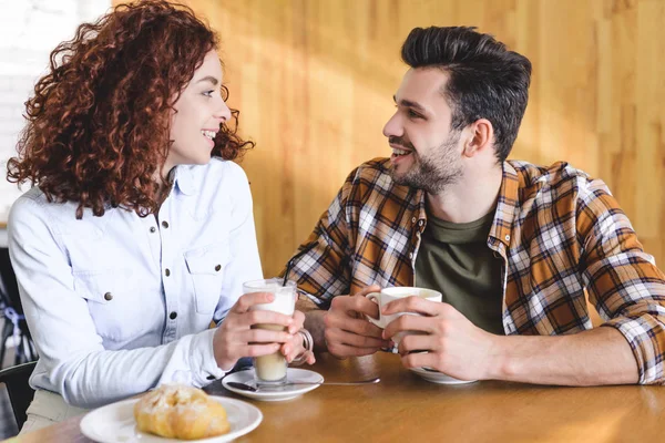 Hermosa y sonriente pareja bebiendo café y mirándose - foto de stock