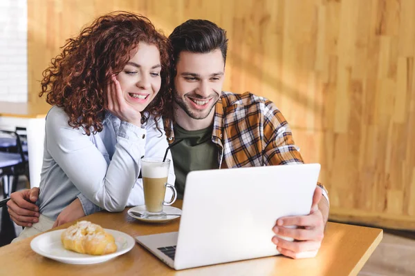 Beautiful woman and handsome man hugging and using laptop at cafe — Stock Photo