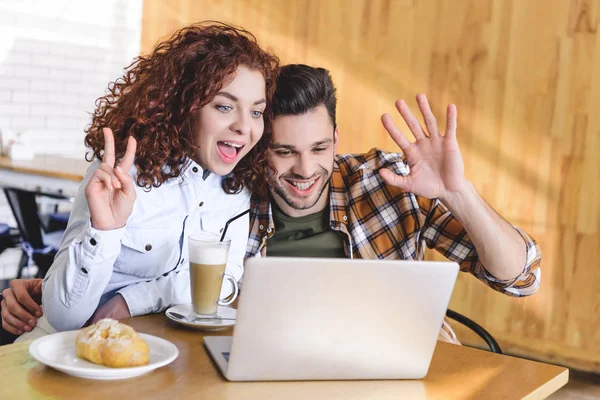 Beautiful woman and handsome man hugging, using laptop and showing gestures — Stock Photo