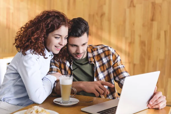 Attractive woman and man hugging and using laptop at cafe — Stock Photo