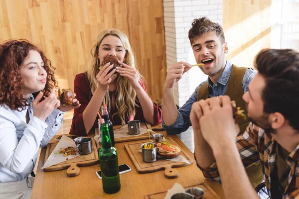 Messa a fuoco selettiva di amici belli e attraenti mangiare gustosi hamburger e patatine fritte — Foto stock