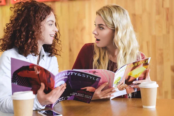 Attraktive und lächelnde Frauen, die Zeitschriften halten und im Café reden — Stockfoto