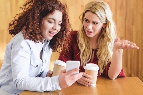 Beautiful women holding paper cups and smartphone at cafe — Stock Photo