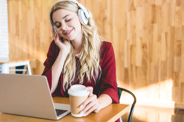 Selective focus of beautiful woman listening music with headphones and holding paper cup — Stock Photo