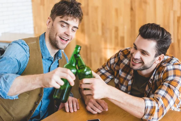 Hombres guapos y sonrientes animando con botellas de vidrio de cerveza - foto de stock