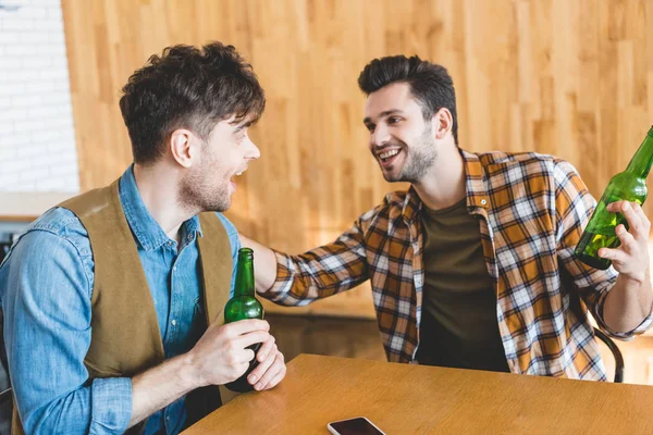 Красивые и улыбающиеся мужчины, держащие стеклянные бутылки пива и разговаривающие — стоковое фото