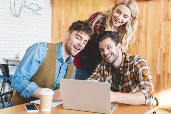 Handsome and beautiful friends using laptop and smiling at cafe — Stock Photo