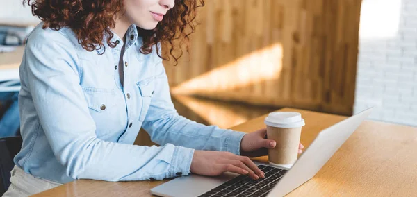 Vista ritagliata della donna in possesso di tazza di carta e utilizzando il computer portatile — Foto stock