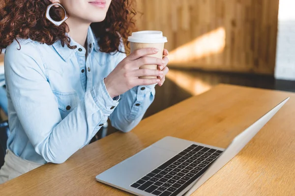 Cropped view of woman holding paper cup with laptop on table — Stock Photo