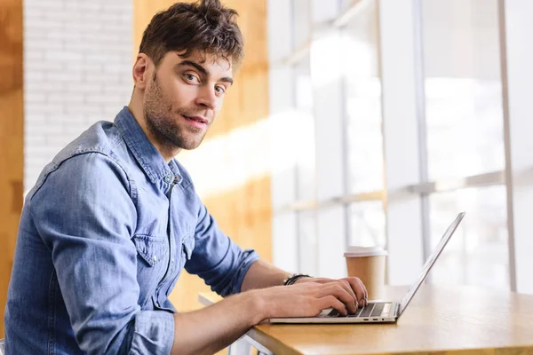 Bell'uomo che usa il computer portatile e guarda la macchina fotografica al caffè — Foto stock