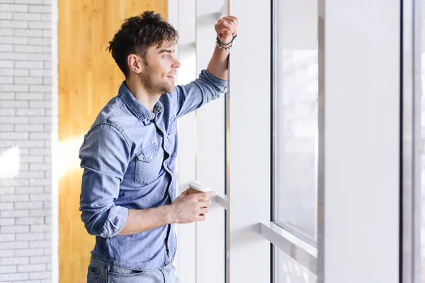 Handsome and smiling man holding paper cup and looking away — Stock Photo