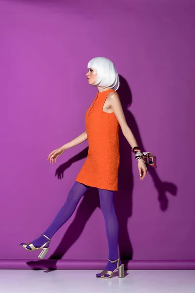 Вид сбоку на молодую женщину в белом парике идущую на фиолетовом фоне — стоковое фото