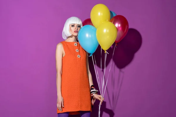 Sensual joven en peluca blanca sosteniendo globos de aire sobre fondo púrpura - foto de stock